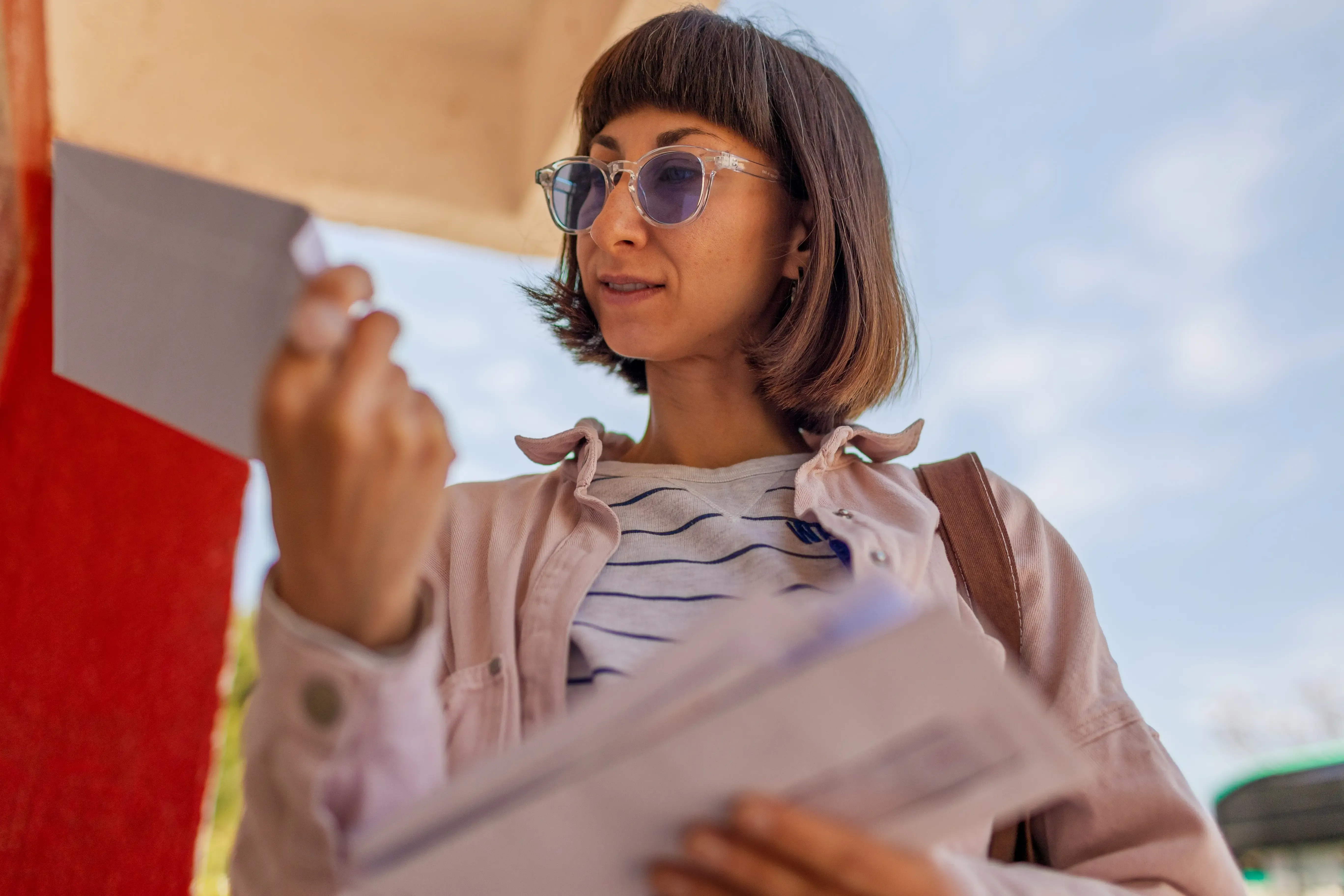 Person standing outdoors reviewing a letter while holding several documents, appearing to read important mail received by post.