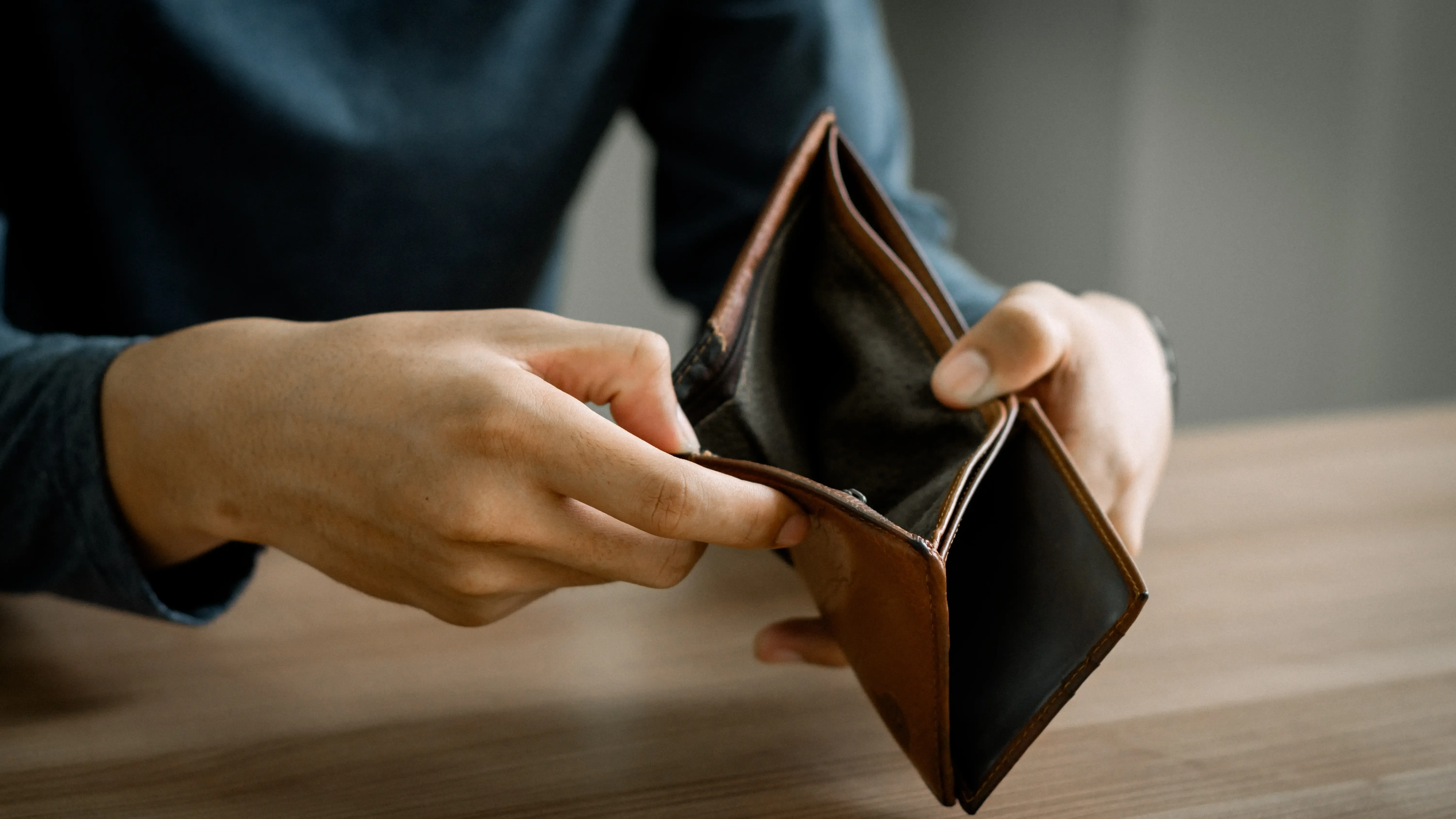 Close‑up of hands opening an empty wallet on a desk.