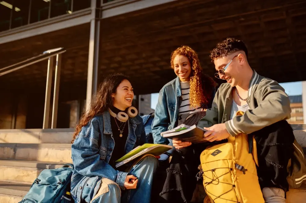 Group of students sitting on outdoor steps, studying together with notebooks, backpacks, and school supplies.