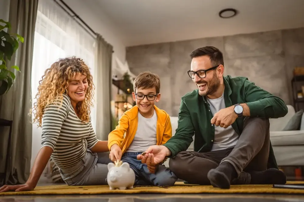 Famille à la maison déposant de la monnaie dans une tirelire, symbolisant des économies et un soutien financier lié au crédit d’impôt du Québec pour l’épicerie et l’énergie en 2026.