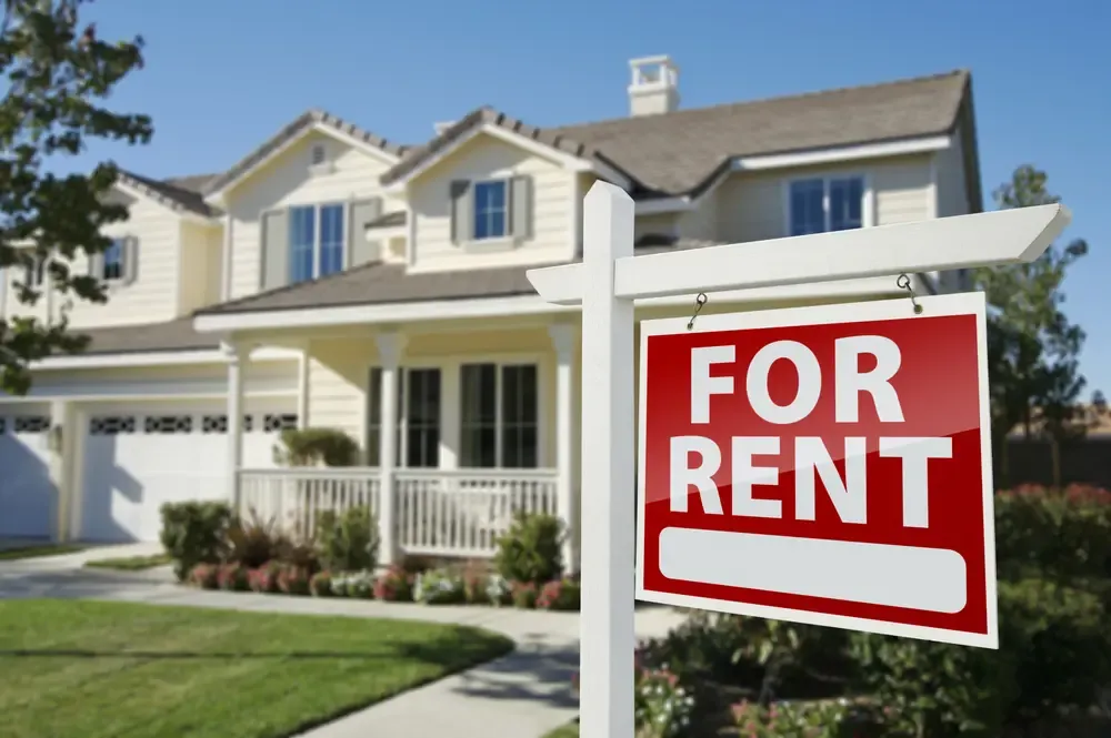 For Rent sign displayed in front of a detached rental home with landscaped yard.