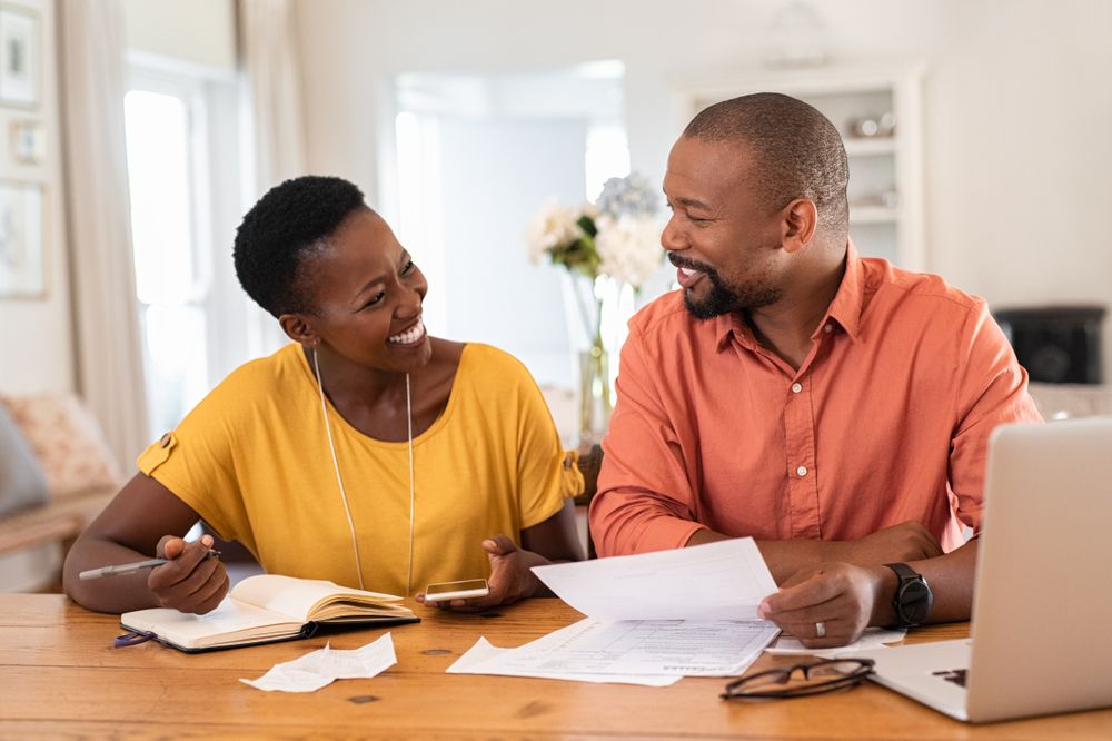 Two people sitting at a table reviewing financial documents together with a notebook, calculator, and laptop.