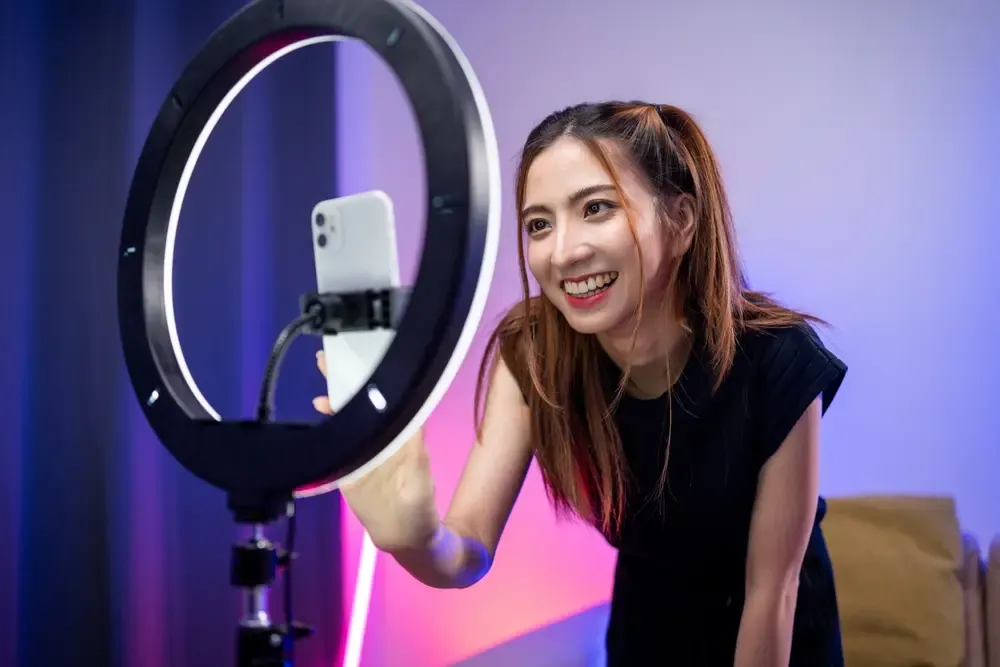 Person filming content with a smartphone mounted in front of a ring light in a home studio setup.